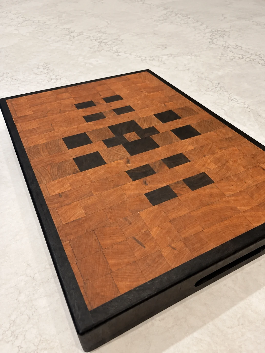 Warm end-grain cutting board with its original dark pixel pattern on a clean stone countertop