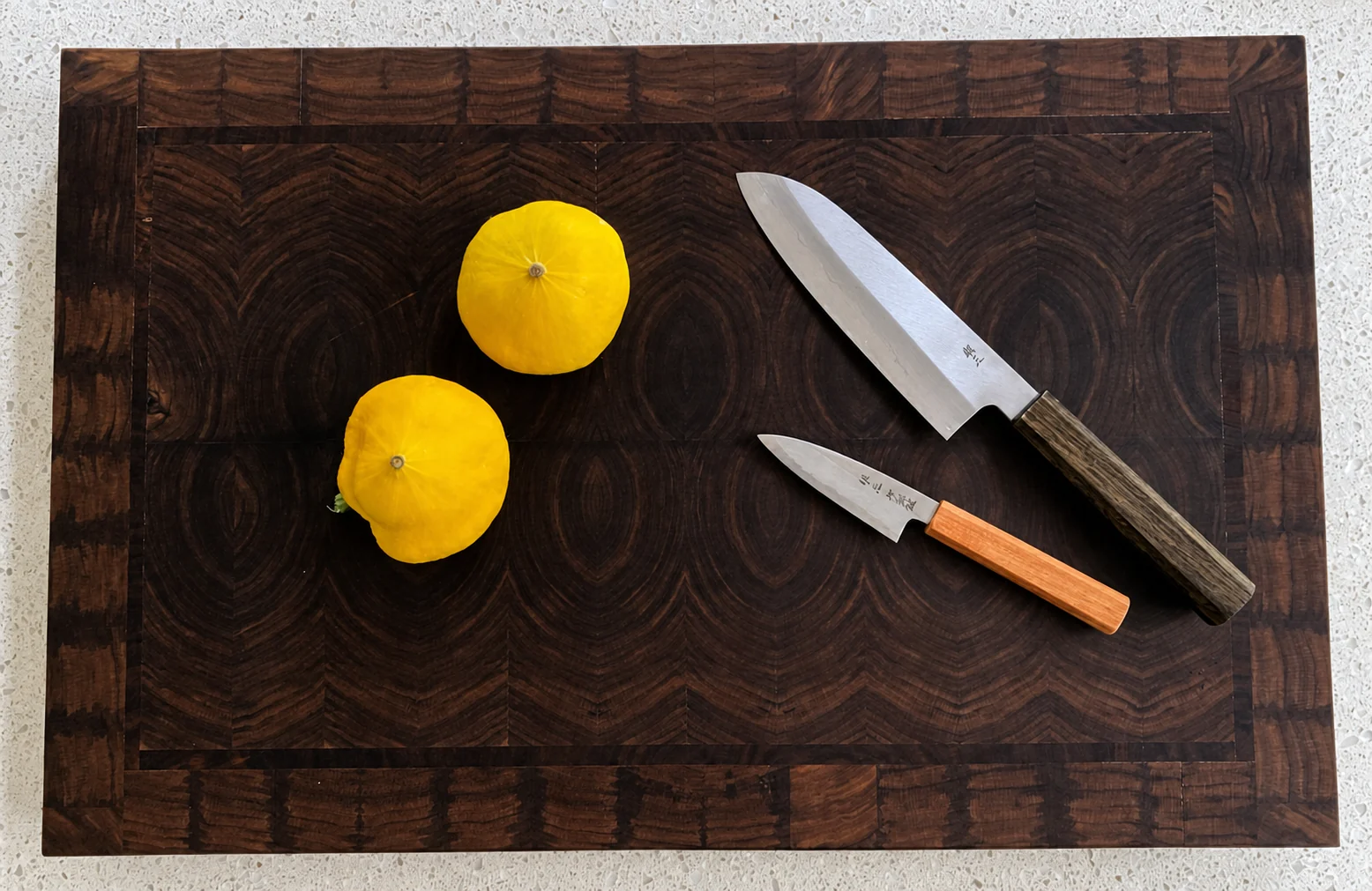 Walnut end-grain cutting board with two knives and yellow squash